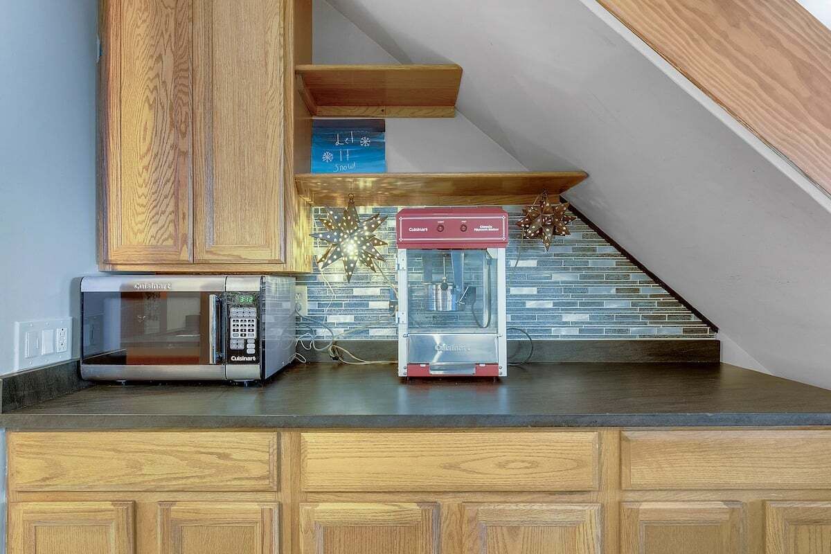 A kitchen with a microwave, a food processor, and a staircase with a tiled wall.