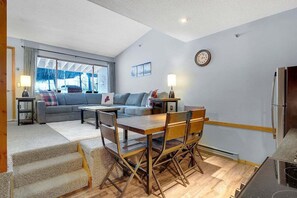 Ein modernes Wohnzimmer mit einer Couch, einem Esstisch, Stühlen und einer Küchenzeile inklusive Kühlschrank.