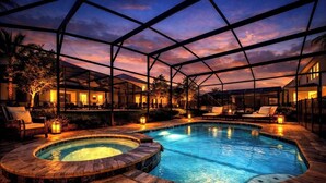 A swimming pool with a hot tub, lounge chairs, and a covered area with a view of the sunset.