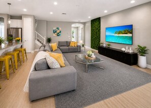 Un salon moderne avec un canapé d’angle gris, une table basse en verre et un grand téléviseur à écran plat.