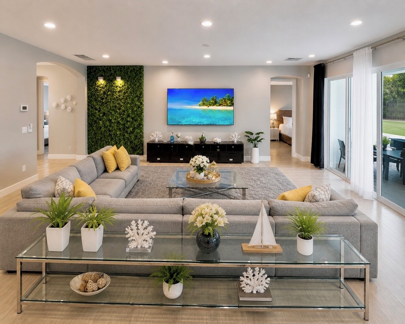 Ein modernes Wohnzimmer mit einem grauen Ecksofa, einem Glastisch und einem an der Wand befestigten Fernseher.