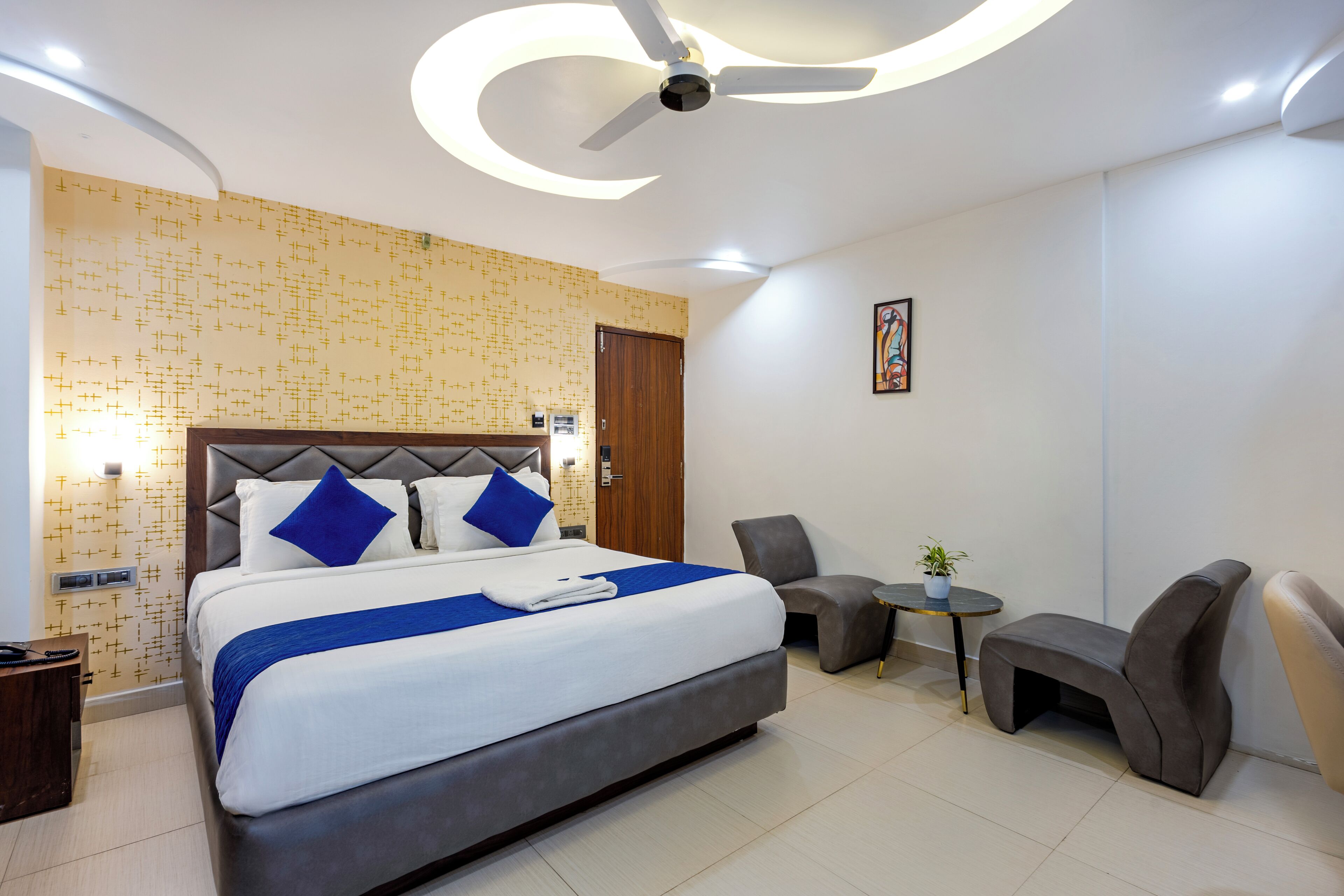 A modern hotel room with a large bed, a ceiling fan, a small round table, and two armchairs.