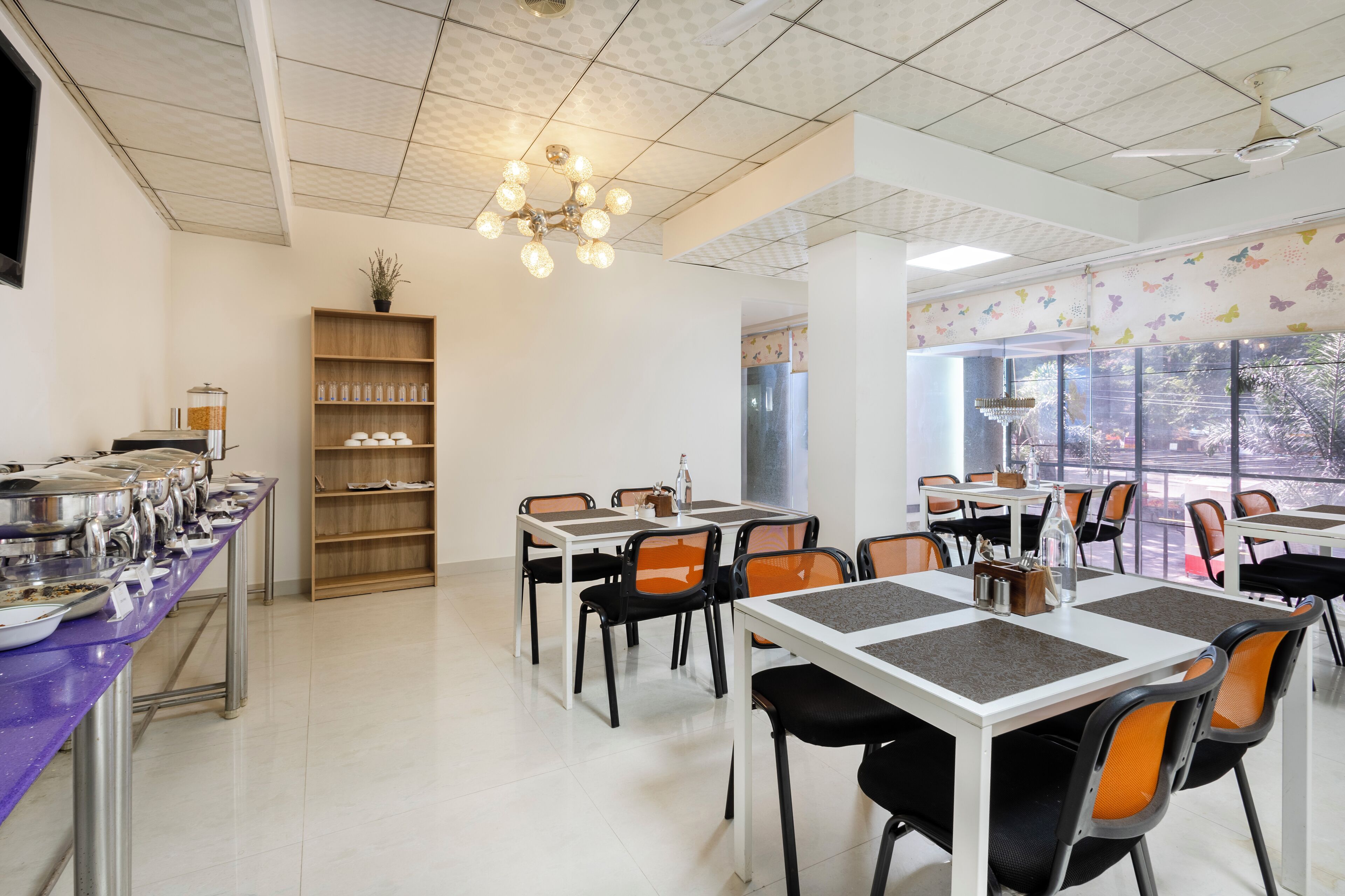 A dining area with multiple tables and chairs, a ceiling fan, and a bookshelf with jars.