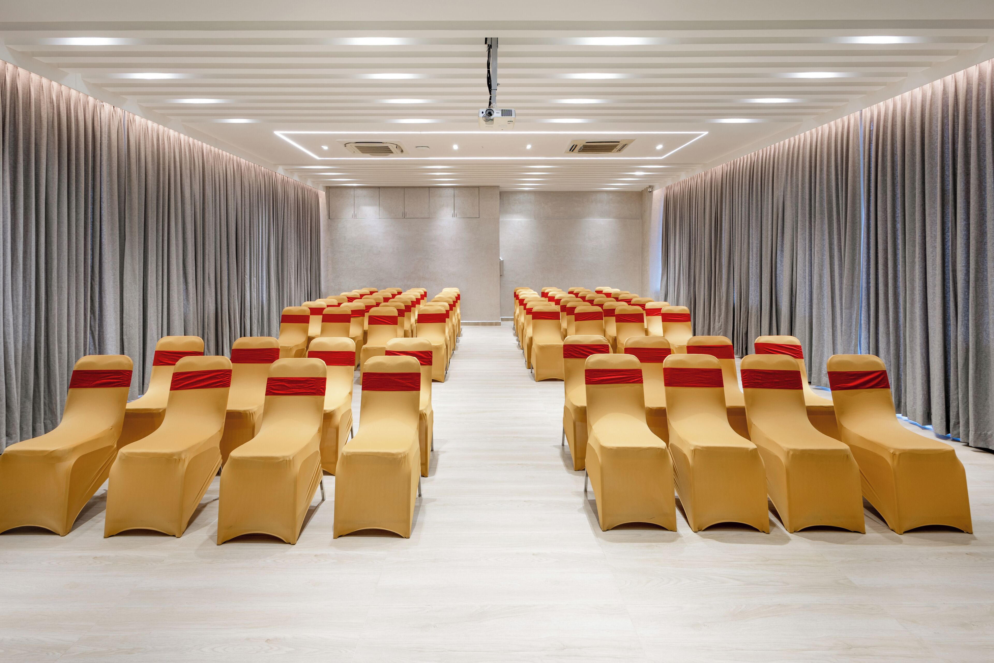 A conference room with rows of beige chairs, grey curtains, and a modern ceiling design.