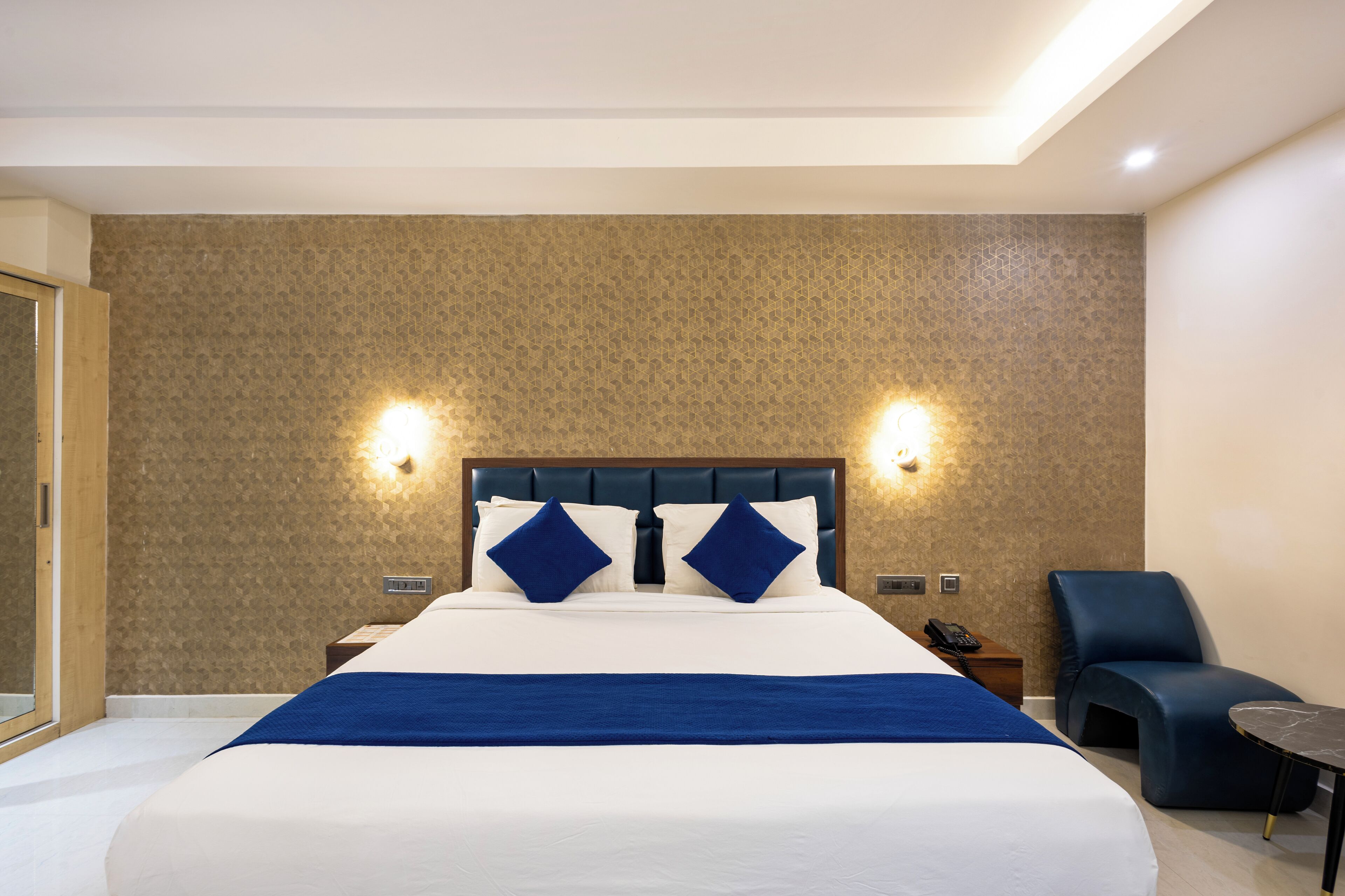 Een hotelkamer met een groot bed, twee nachtkastjes, een stoel en een klein tafeltje.