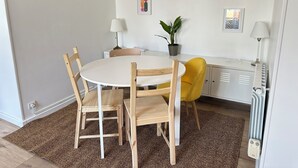 Un coin repas avec une table ronde, des chaises en bois, une chaise jaune, une plante en pot et des œuvres d’art mural.