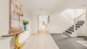Un couloir moderne avec un escalier, une console décorative et un grand tableau abstrait.