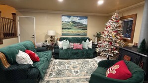 Ein Wohnzimmer mit grünen Sofas, einem Weihnachtsbaum und einem Gemälde an der Wand.
