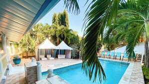 Una piscina amb solàrium enrajolat, gandules i una zona de seients coberta amb tòtems blancs.