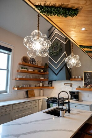 A modern kitchen with marble countertops, a built-in stove, and hanging spherical light fixtures. - Modern Organic Country Home w/ Hot Tub, Pet Friendly, Near USAFA (Colorado Springs)