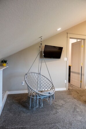 A room with a hanging chair, a mounted TV, and a door leading to another room. - Modern Organic Country Home w/ Hot Tub, Pet Friendly, Near USAFA (Colorado Springs)
