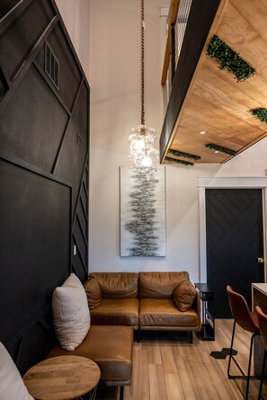 A modern interior with a brown leather sofa, a wooden dining table, and a hanging light fixture. - Modern Organic Country Home w/ Hot Tub, Pet Friendly, Near USAFA (Colorado Springs)