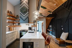 A modern kitchen with a central island, wooden shelves, and a chandelier. - Modern Organic Country Home w/ Hot Tub, Pet Friendly, Near USAFA (Colorado Springs)