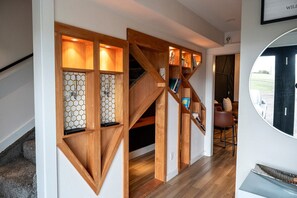 A modern interior with a wooden staircase, hexagonal patterned shelves, and a view through a circular window. - Modern Organic Country Home w/ Hot Tub, Pet Friendly, Near USAFA (Colorado Springs)