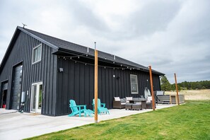 A modern black building with a patio area featuring outdoor furniture and a string of lights. - Modern Organic Country Home w/ Hot Tub, Pet Friendly, Near USAFA (Colorado Springs)