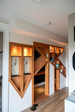 A modern interior with a wooden staircase, built-in bookshelves, and a hexagonal patterned wall. - Modern Organic Country Home w/ Hot Tub, Pet Friendly, Near USAFA (Colorado Springs)