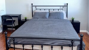 Una cama con estructura metálica, un escritorio y dos pequeñas macetas.