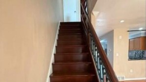 Una escalera de madera con barandilla que lleva a una puerta en la parte superior.