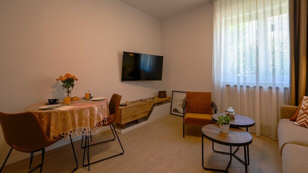 A modern living room with a dining area, a flat-screen TV mounted on the wall, and a large window with sheer curtains. - Modern and Stylish Apartment With Terrace (Rovinj)