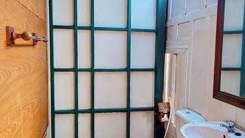 A small, narrow bathroom with a wooden door, a white toilet, and a sink with a mirror.
