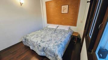 A bedroom with a wooden headboard, a bed with floral bedding, a nightstand, and a window with a view.