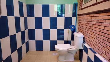 Un baño pequeño con azulejos, un inodoro, un pared de cuadros azules y blancos, y suelo de baldosas.