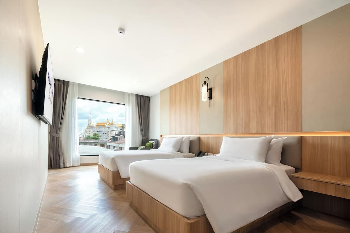 A hotel room with two beds, a TV, a view of a cityscape, and a wooden floor.
