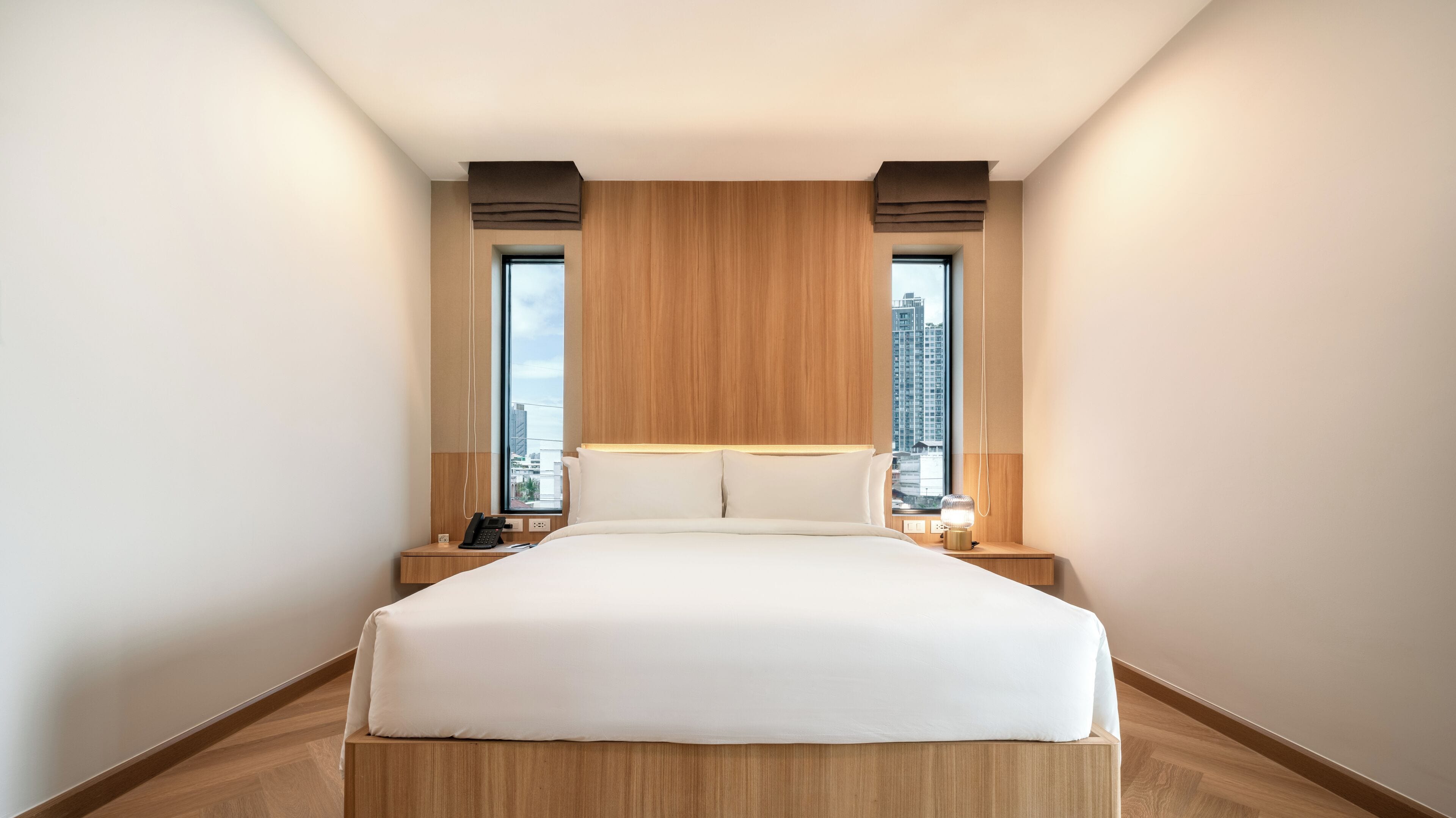A modern hotel room with a large bed, two bedside tables, a city view, and a wooden headboard.