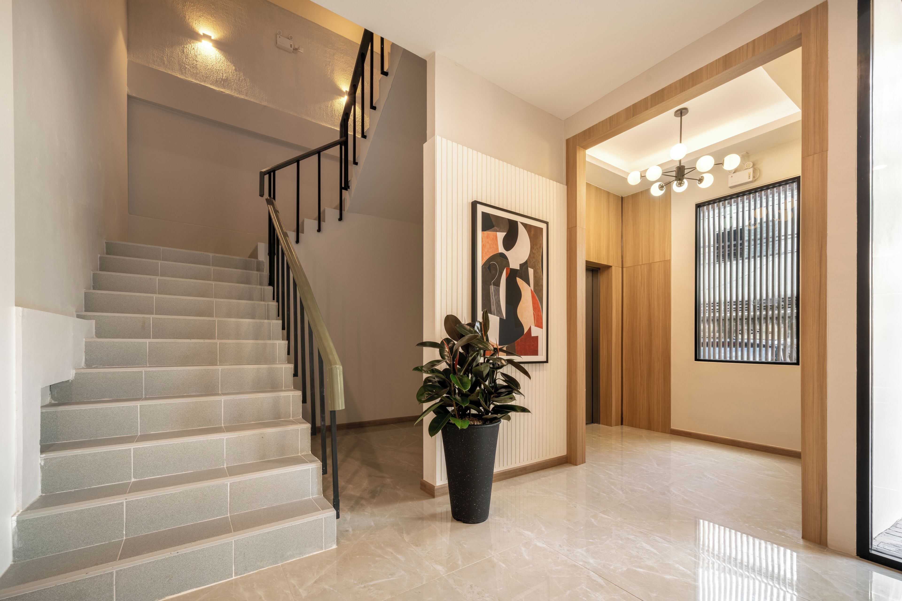 A modern interior with a staircase, a potted plant, a framed artwork, and a window with blinds.