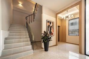 Un interior moderno con una escalera, una planta en maceta, una obra de arte enmarcada y una ventana con persianas.