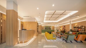 A modern hotel lobby with a reception desk, seating area, and a green wall with a decorative element. - Adelphi Itsaraphap (Bangkok)