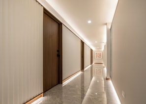 Un pasillo de hotel con puertas de madera, suelo de mármol y una obra enmarcada en la pared.