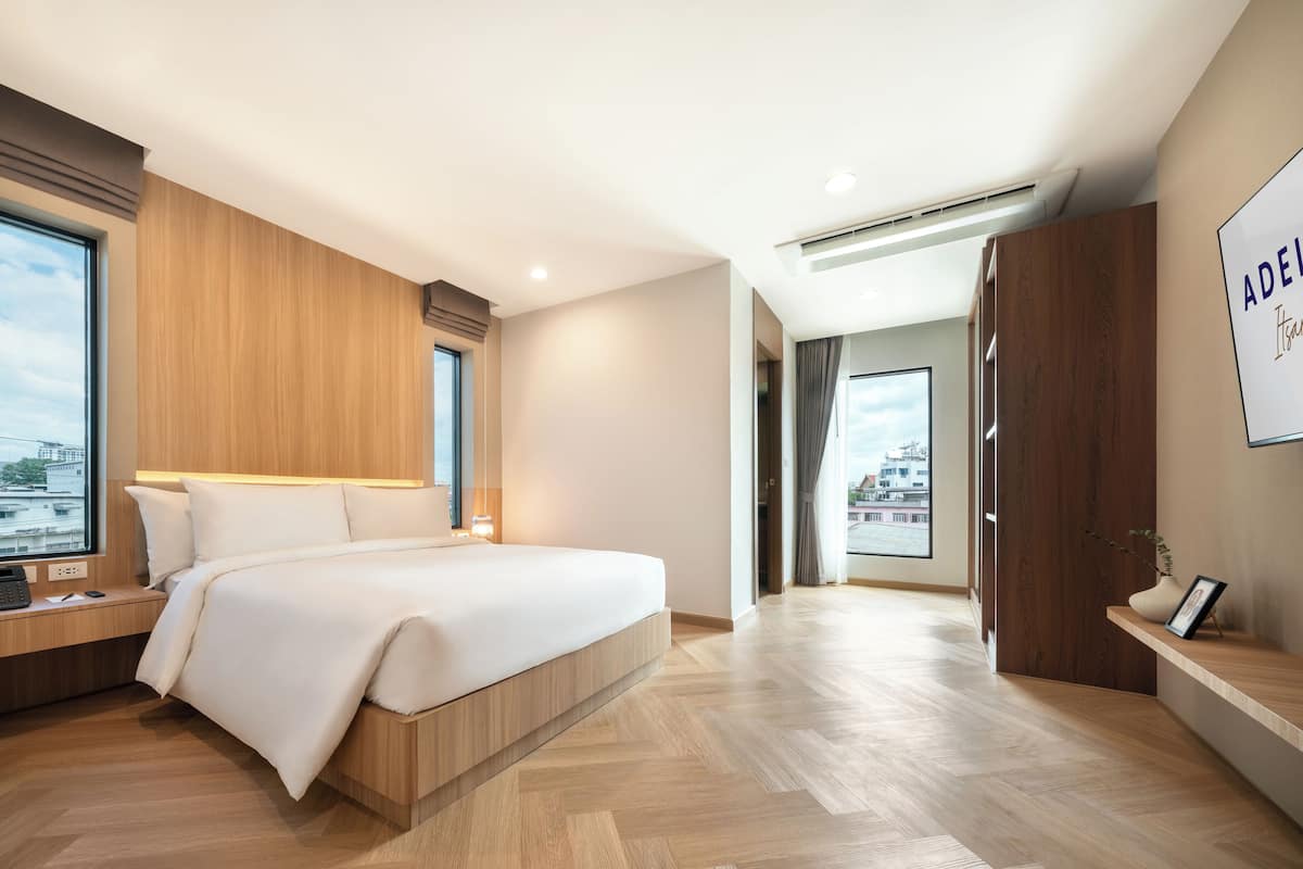 A modern hotel room with a large bed, wooden paneling, a desk with a phone, and a city view.