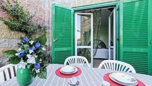 Een eetgedeelte met een tafel gedekt voor twee personen, groene luiken en een potplant met blauwe bloemen.
