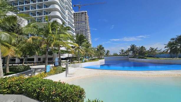 Ein modernes Hotel mit großem Pool, Palmen und Blick auf den Strand.