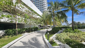 Ein moderner Hotelkorridor mit gewundener Wegeführung, Palmen und blauem Himmel.