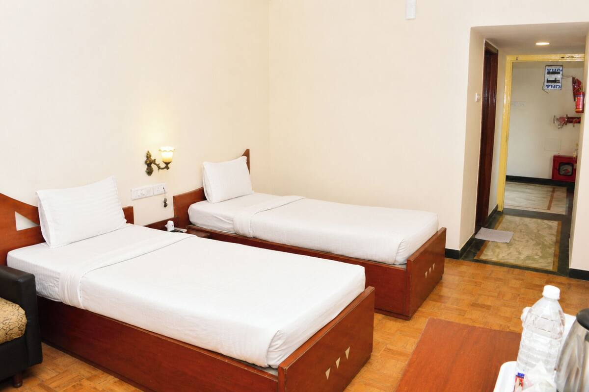 A hotel room with two single beds, a wooden nightstand, a lamp, and a small table with a bottle.