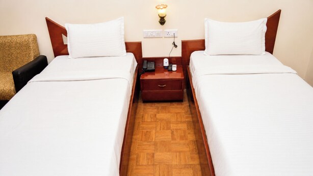 A hotel room with two single beds, a wooden floor, a nightstand with a phone and a lamp, and a wall socket. - Hotel Satlaj Raipur (Raipur)