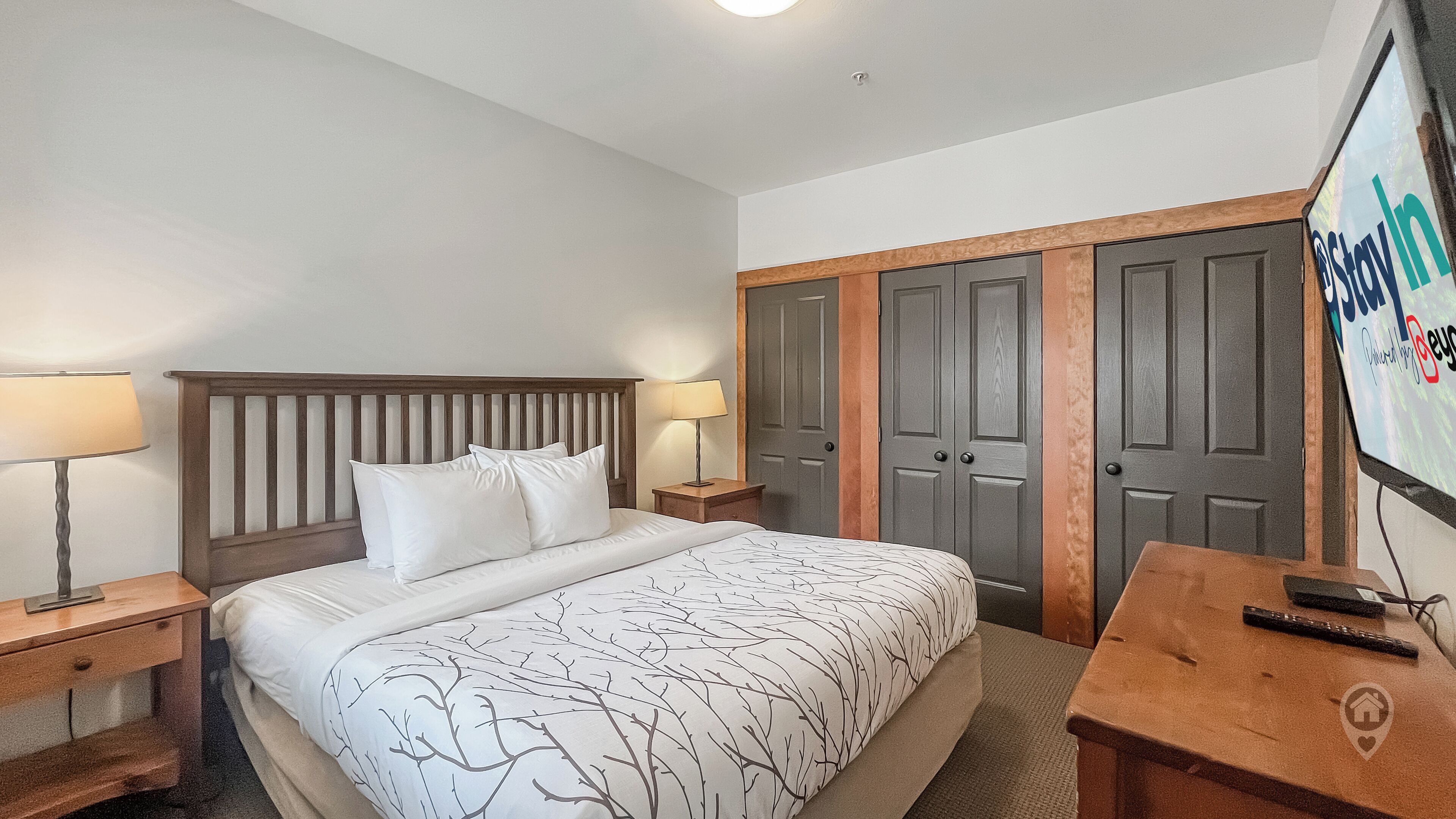 Une chambre d’hôtel comprenant un lit, deux tables de chevet, une lampe, un téléviseur et une armoire.