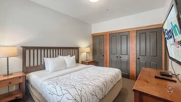 Une chambre d’hôtel comprenant un lit, deux tables de chevet, une lampe, un téléviseur et une armoire.