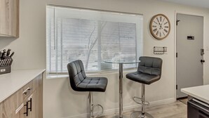 Una cocina moderna con dos taburetes de bar, una mesa con cubierta de vidrio y un reloj en la pared.