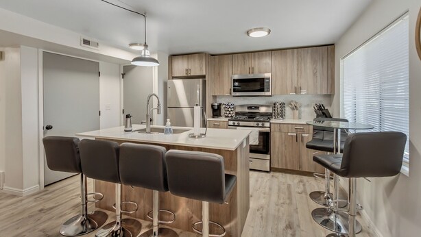 Una cocina moderna con una isla central, taburetes de bar, electrodomésticos de acero inoxidable y armarios de madera.