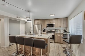 A modern kitchen with a central island, bar stools, stainless steel appliances, and wooden cabinets. - Cozy 2BR/1BA Downtown SLC stay with fast Wi-Fi & great location (Salt Lake City)