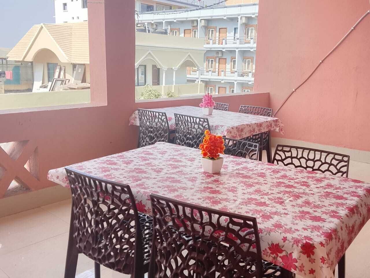 Un balcon avec une table et des chaises, un vase de fleurs et une vue sur les bâtiments en arrière-plan.