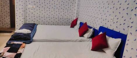 Una habitación con dos camas, cada una con ropa blanca y almohadas rojas, y un cabecero azul.