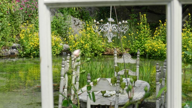 A rustic outdoor seating area with a stone table and chairs, surrounded by a pond and lush greenery. - CHAMBRE-GÎTE LES TOURTEREAUX EN ISERE (LE VERCORS) (Saint-Just-de-Claix)