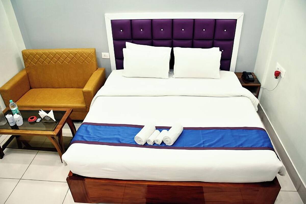 Une chambre d’hôtel comprenant un lit, une chaise, une petite table avec des articles de toilette et une table de chevet avec un téléphone.