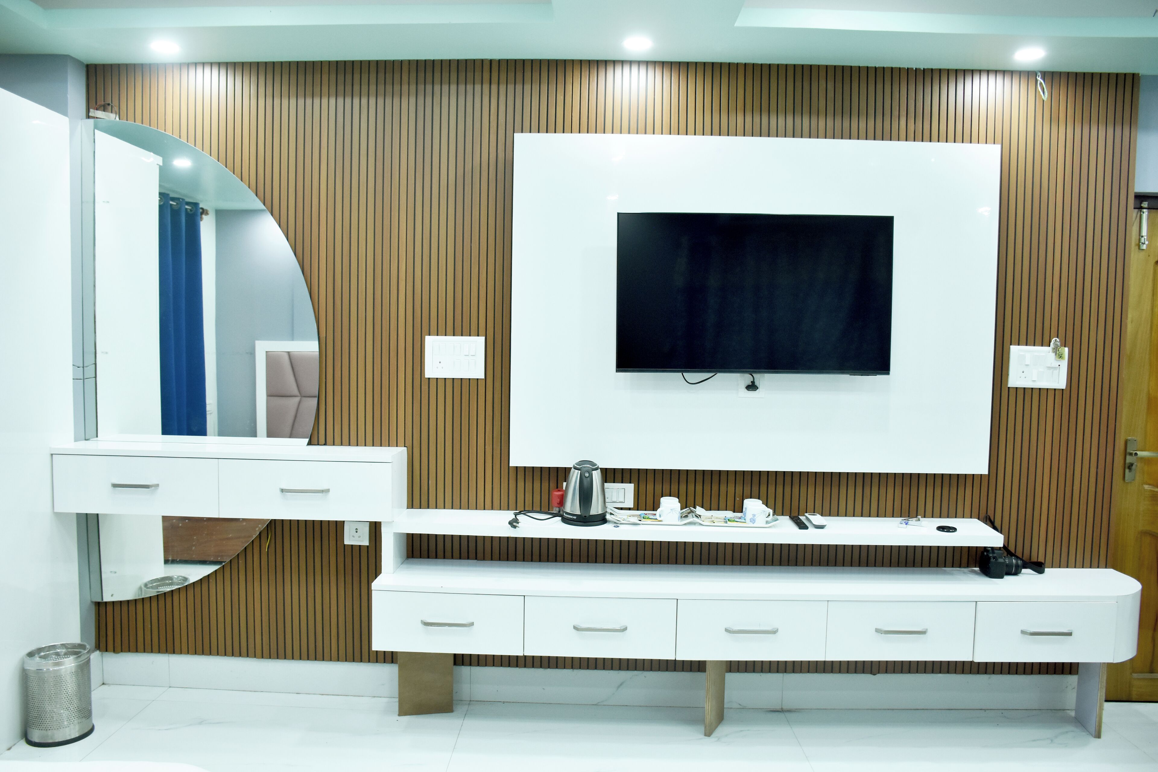 A modern bathroom with a large mirror, a vanity with drawers, a mounted TV, and a wooden panel wall.