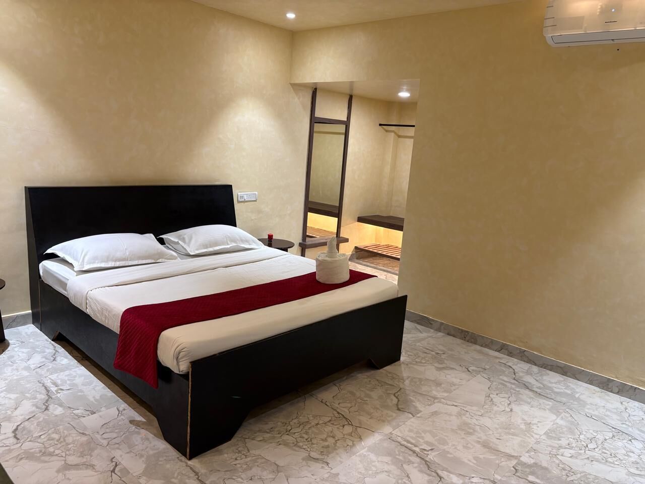 A modern hotel room with a large bed, a red throw blanket, and a marble floor.
