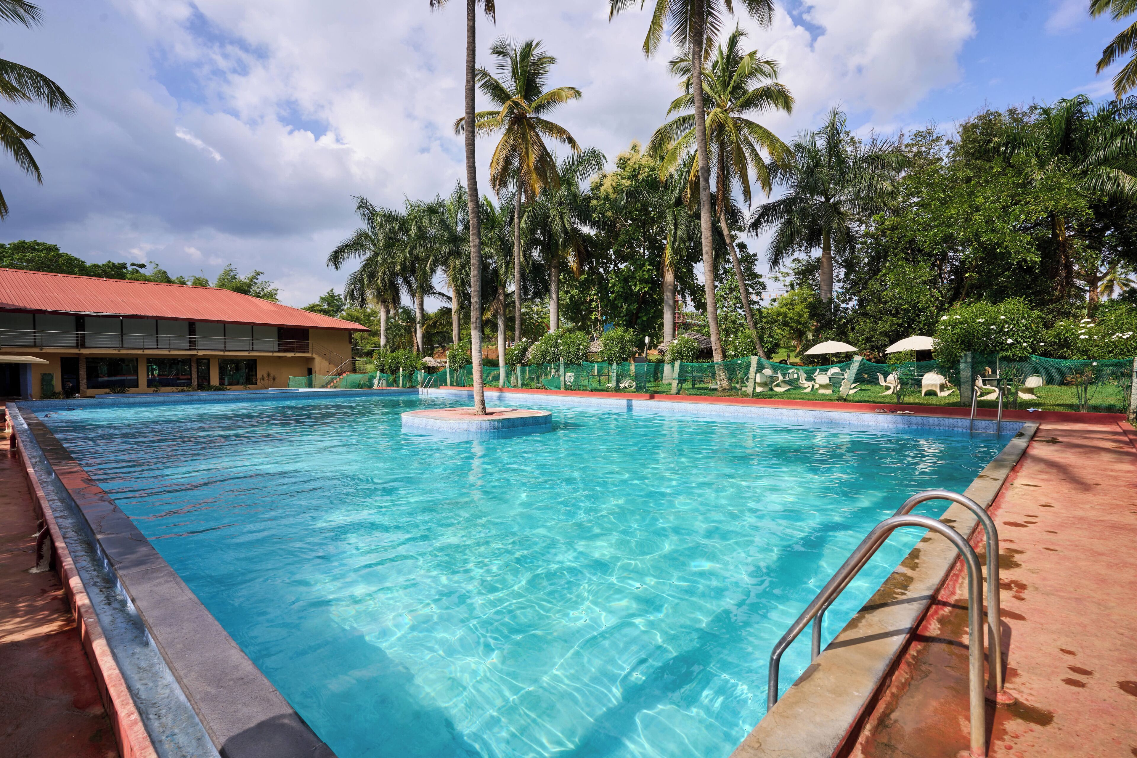 A clear blue swimming pool with a palm tree in the center, surrounded by a fence and lounge chairs.
